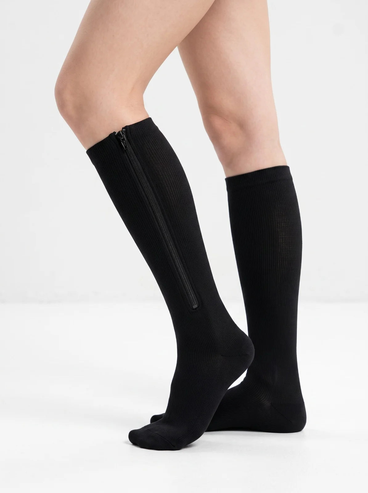 Black knee-high compression socks with a side zipper, shown on a model's legs against a white studio background. 